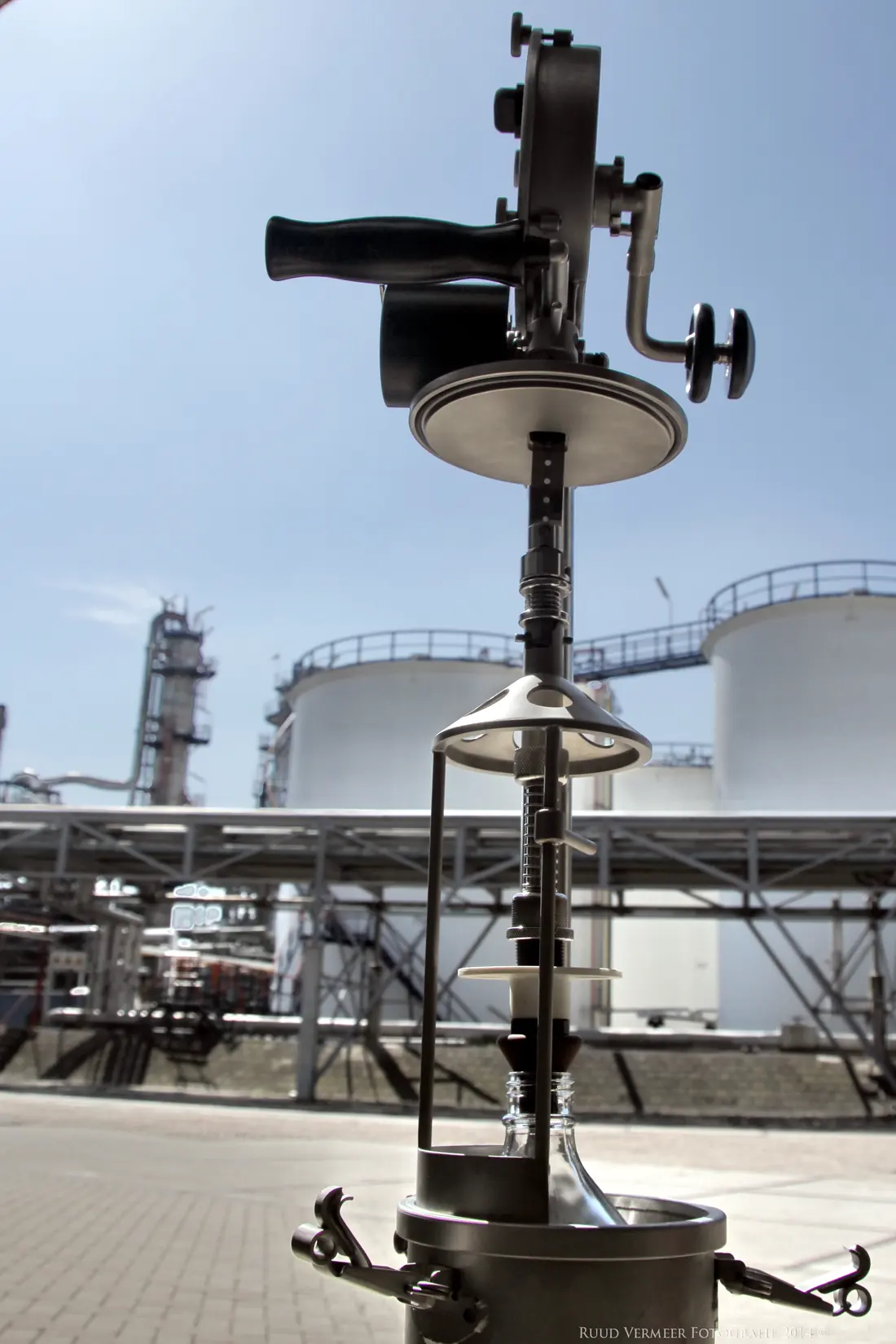 A UKSGL sampling winder, sampler and bottle standing in front of refinery storage tanks